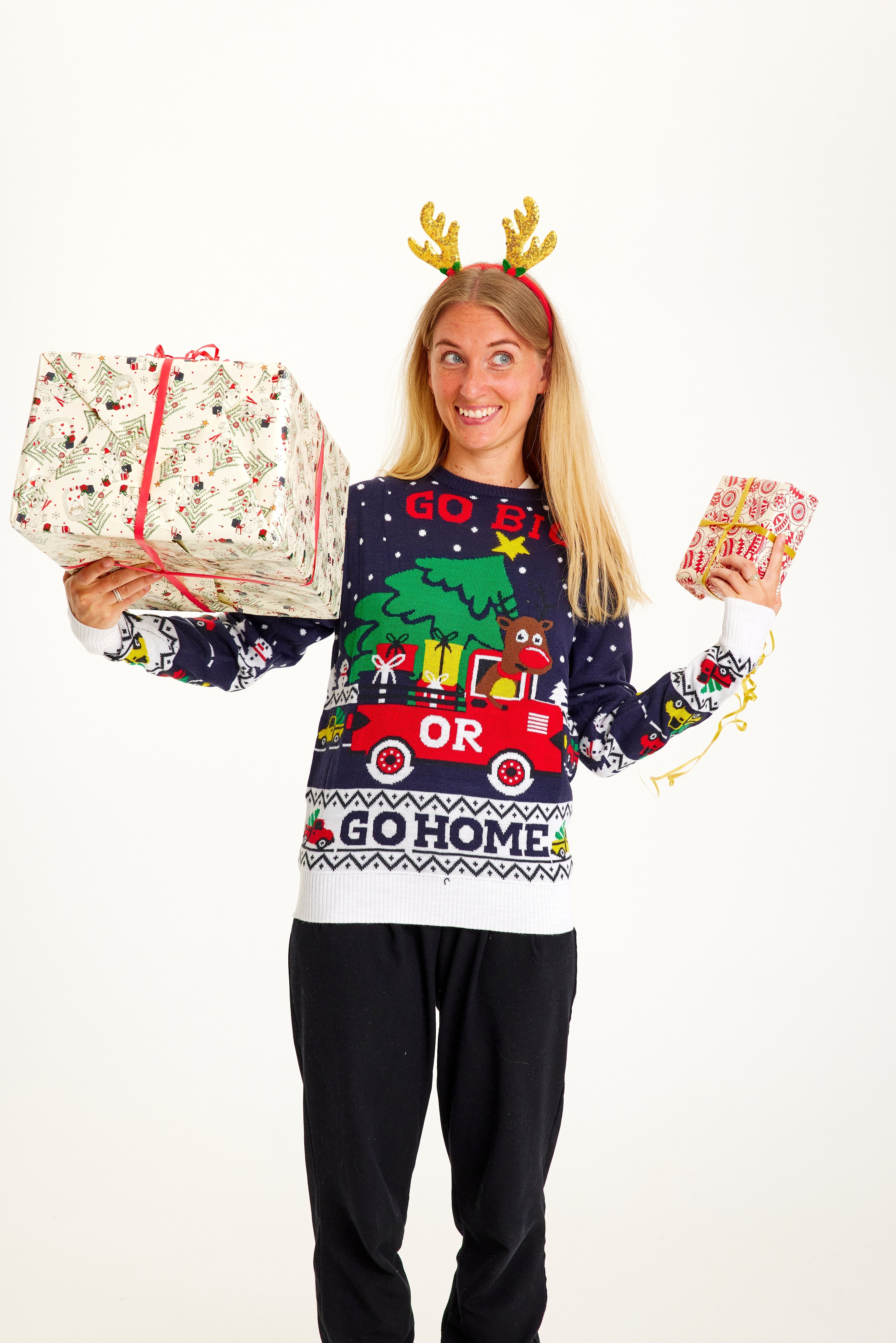 Eine Frau mit Weihnachtsgeschenken, die einen weiß-blauen Weihnachtspullover trägt.